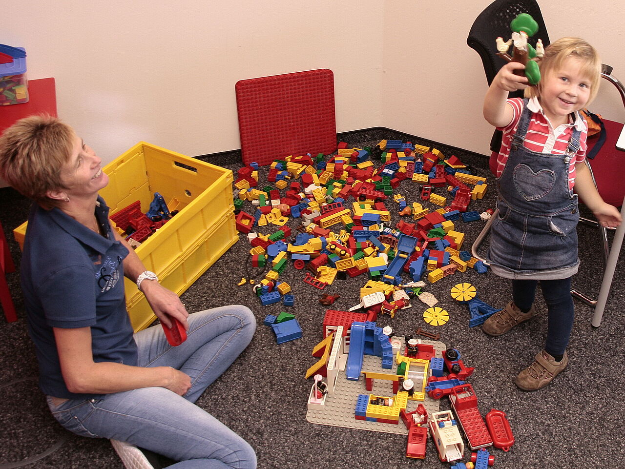 Familienfreundlichkeit bei CONTAG: Eine Mitarbeiterin spielt mit einem kleinen Mädchen in der betriebseigenen Spielecke mit bunten Bausteinen.