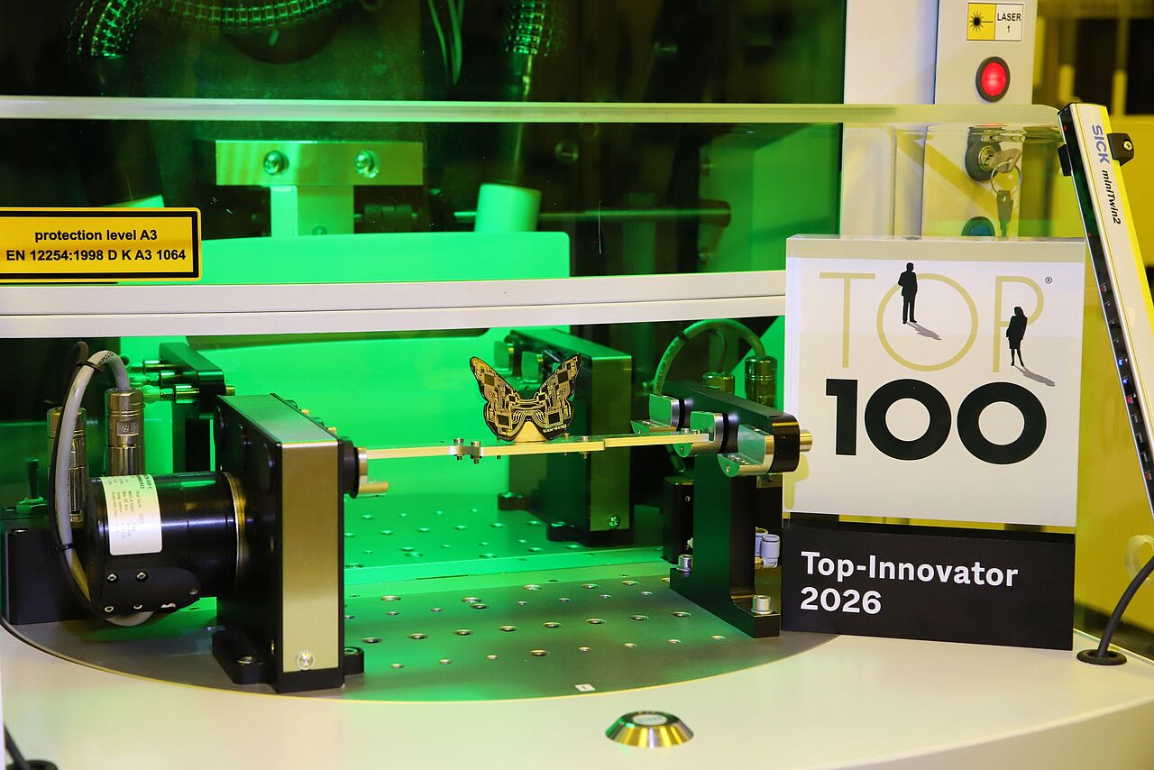 Auszeichnung für CONTAG: Das Siegel „Top 100 Innovator 2026“ neben einer hochpräzisen Fertigungsanlage, in der ein filigraner 3D-MID Leiterplatten-Schmetterling bearbeitet wird.