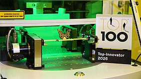 Auszeichnung für CONTAG: Das Siegel „Top 100 Innovator 2026“ neben einer hochpräzisen Fertigungsanlage, in der ein filigraner 3D-MID Leiterplatten-Schmetterling bearbeitet wird.