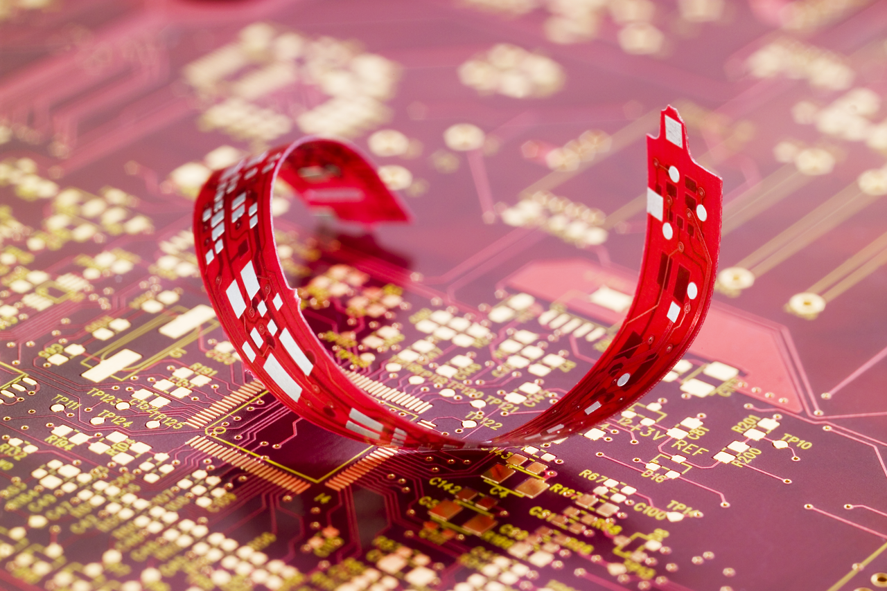 Nahaufnahme einer spiralförmig gebogenen roten Leiterplatte aus dünnem FR4-Substrat von CONTAG, liegend auf einer größeren Platine.