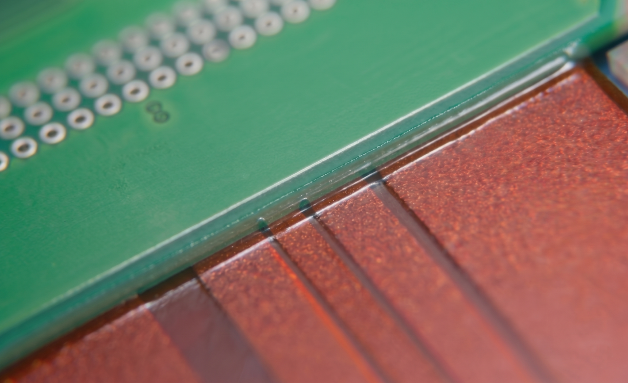 Nahaufnahme der Kantenversiegelung am Übergang zwischen starrem und flexiblem Teil einer CONTAG Leiterplatte, realisiert durch einen semi-flexiblen 2k-Kleber zum Schutz vor mechanischer Belastung.