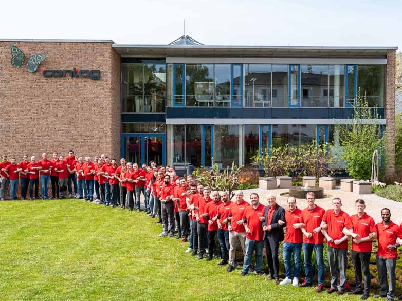 Bewerbung bei CONTAG: Die Belegschaft in roten Firmen-Shirts steht als starkes Team aufgereiht vor dem Hauptgebäude in Berlin.