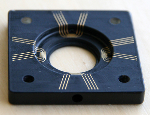 Ein schwarzer, quadratischer 3D-MID Schaltungsträger von CONTAG, hergestellt im LDS-Verfahren, mit präzise geführten goldenen Leiterbahnen über verschiedene Ebenen und Vertiefungen.